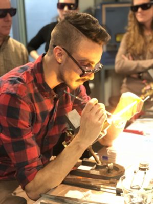 An artist uses a torch to sculpt rods of clear glass